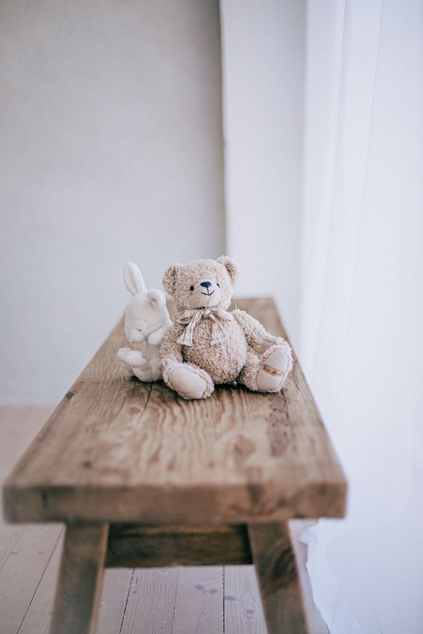 Teddy bear and rabbit plush toys sitting on a rustic wooden table