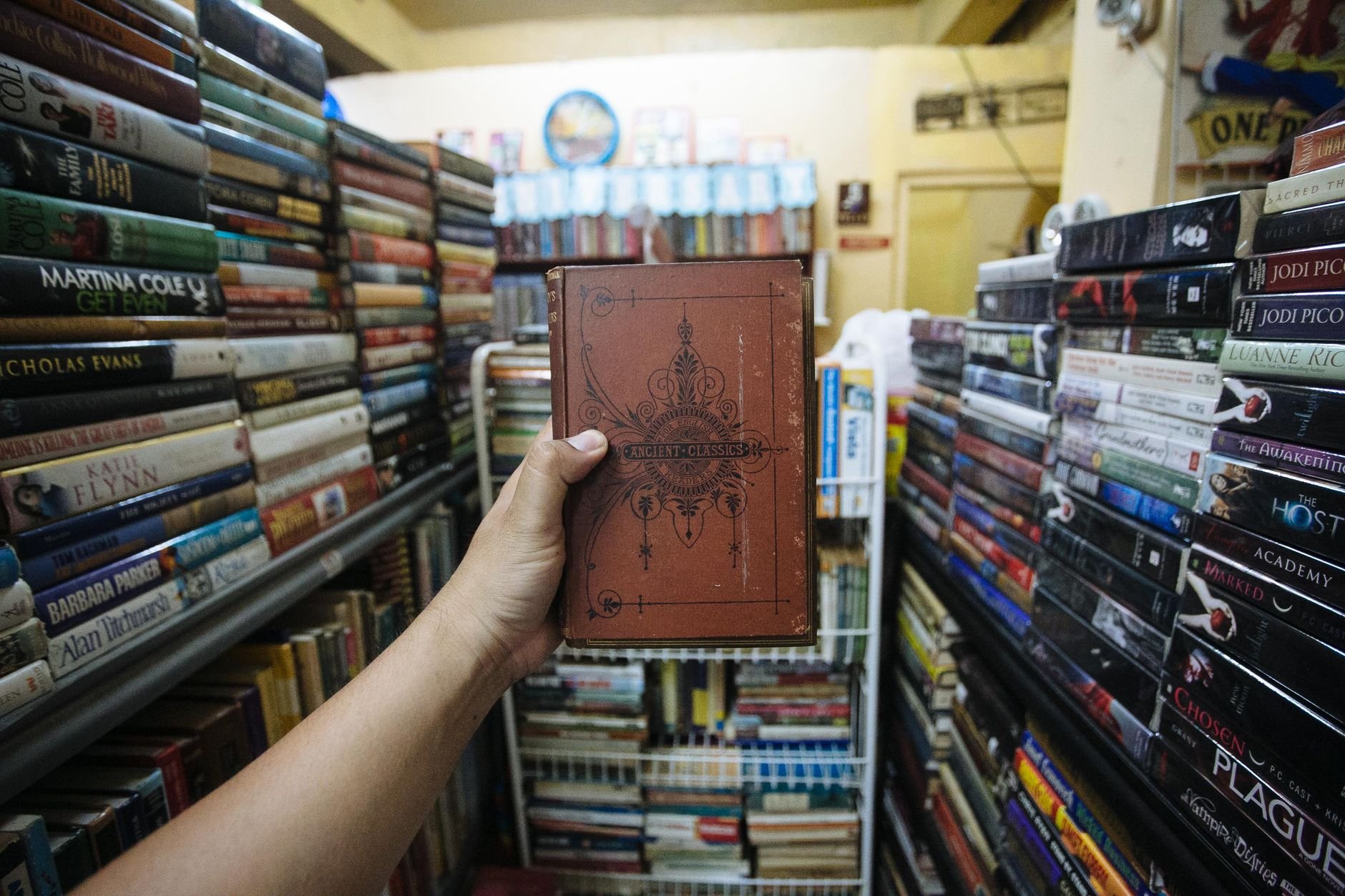 A hand holding a vintage book amidst shelves filled with books in a cosy bookstore